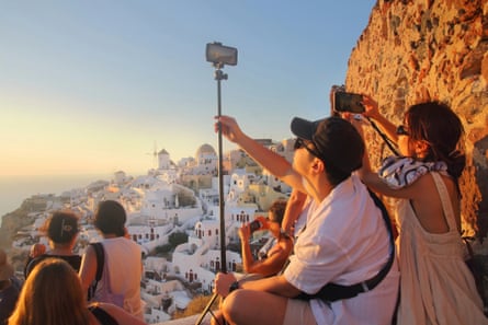 Tourists capture a sunset in Oia village on the Greek island of Santorini.