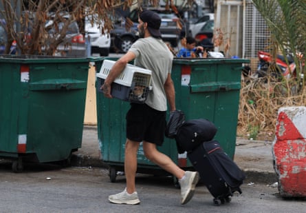 A man with luggage and a cat in a carrier walks through a street