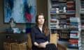 Photograph of author Elif Shafak sitting in a chair in her home looking out of a window, behind her is a bookcase and some artwork