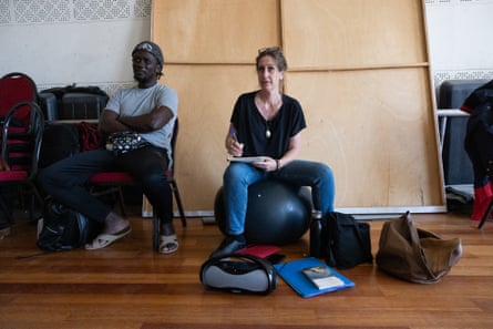A European woman sitting next to an African man writes while watching something off-camera