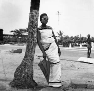 Miss Biney leaning against a coconut tree in front of James Fort prison, Jamestown, Accra, c1953