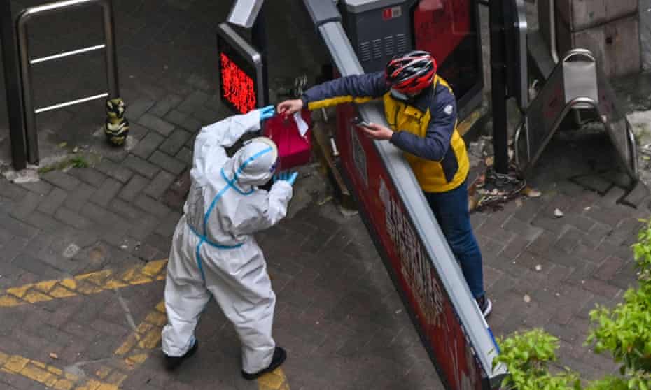 A worker wearing protective gear receives an item from a delivery worker in Shanghai.