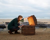 A woman looks inside a treasure chest with gold on a deserted beach.