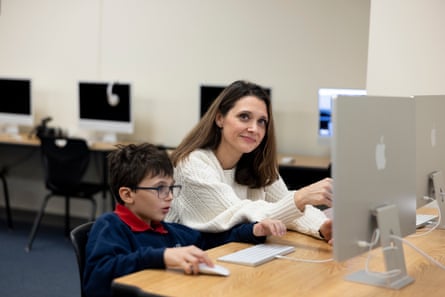 امرأة وصبي يجلسان أمام جهاز كمبيوتر في معمل كمبيوتر.