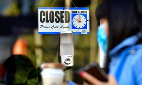 Woman walks past a closed sign hanging on the door of a small business in Los Angeles