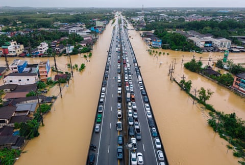 Vehicles parked on an elevated road surrounded by floodwaters