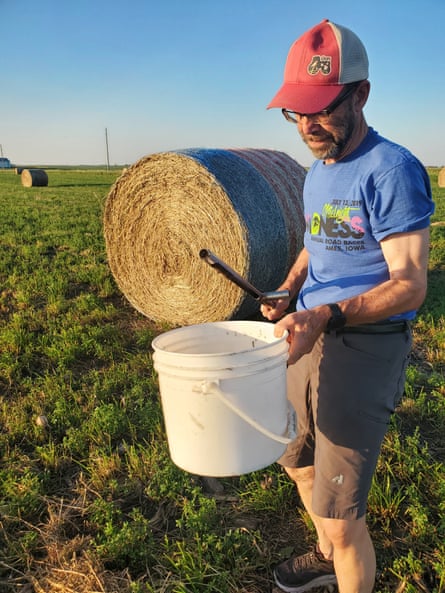 A man in shorts standing near a hay bale in a field
