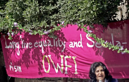 A middle-aged Arab woman speaking into a microphone before a banner that says ‘Long live equality and secularism’ and ‘OWFI’