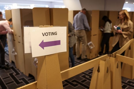A sign saying ‘voting’ with a purple arrow on it and voters casting their ballots at cardboard booths ahead of the national election at an Australian Electoral Commission