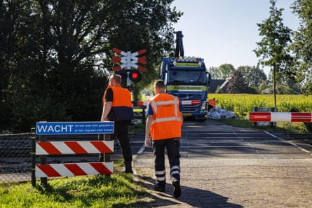 Two men in hi-vis waistcoats alongside a level crossing, with a truck parked opposite