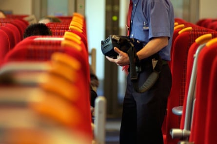 Ticket inspector with machine on train with orange seats.