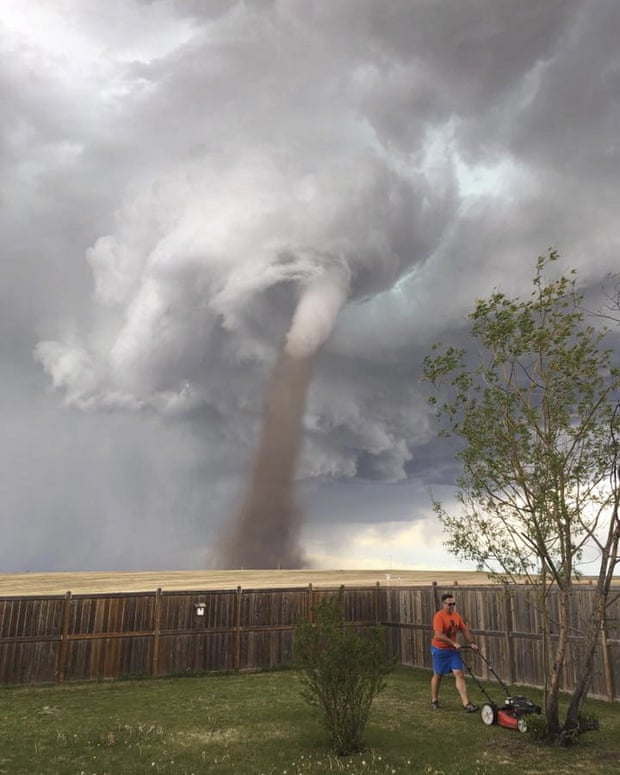 Theunis Wessels mows his lawn at his home in Three Hills, Alberta, as a tornado swirls in the background.