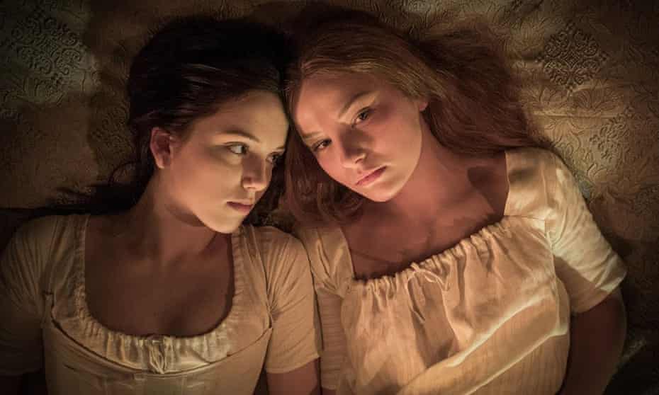 Devrim Lingnau and Hannah Rae lie side by side in a candlelit bedroom in Carmilla