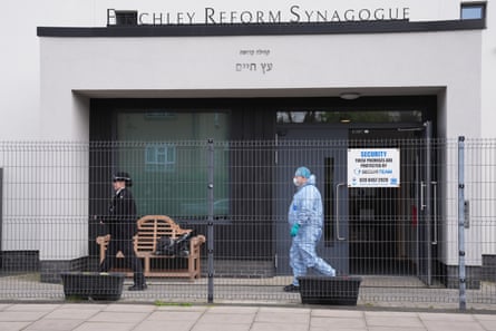 A police officer and forensic officer in blue hazmat suit outside Finchley Reform Synagogue