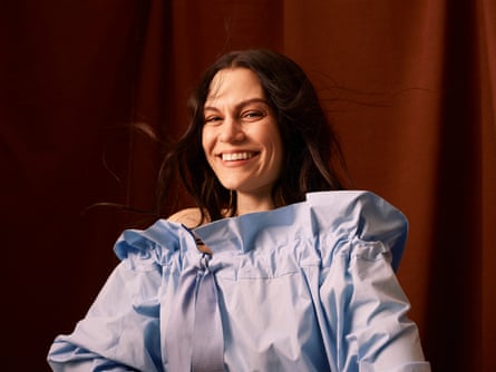 Jessie J pictured from just below the waist up, smiling at the camera, wearing a pale-blue blouse with long sleeves and an open ruffled neck with a pale-blue bow on her right-hand side