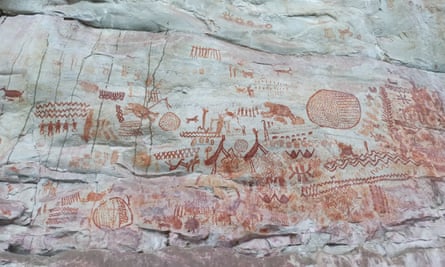 Detailed paintings on a cliff face in red ochre showing human and animal figures, plus geometric patterns