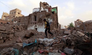 A Yemeni boy runs past buildings damaged by air strikes
