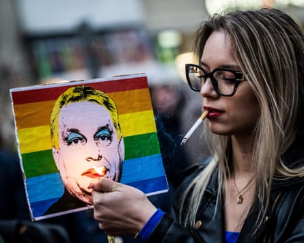 A Pride attender holds a lighter up to a rainbow-streaked depiction of Viktor Orbán.