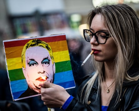 A woman lights a cigarette placed in a placard depicting Hungary’s prime minister, Viktor Orban, wearing makeup and with his head imposed on a Pride flag