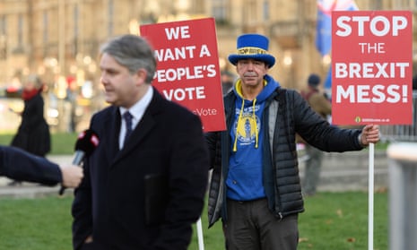 Anti-Brexit protester Steve Bray holds two of his placards as Conservative MP Philip Davies conducts a TV interview on College Green, outside the Houses of Parliament.