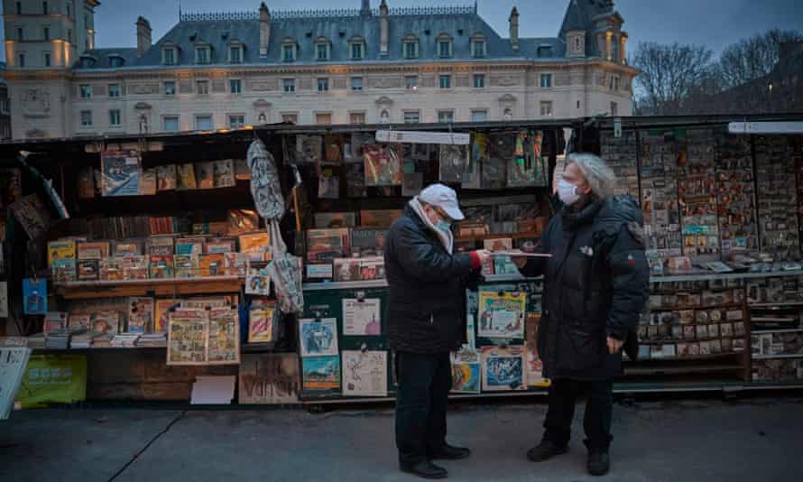 Fancis, who celebrates working as a Bouquiniste for 40 years this year (right), talks to a customer at his book stall on the Seine on 3 January 2021.