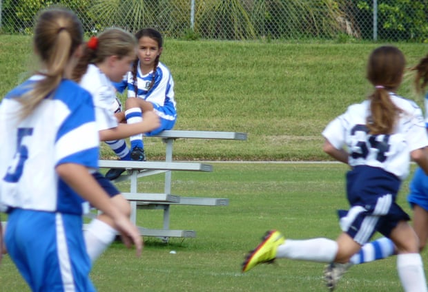 Jazz Jennings sitting on a bench while kids play soccer