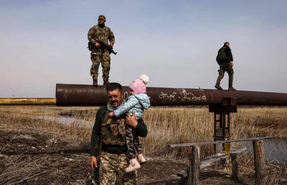 A Ukrainian serviceman carries a child across a river on his shoulder