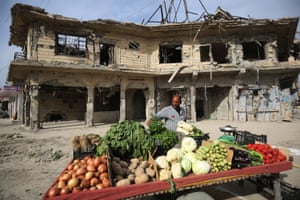 An Iraqi man sells vegetables in front of a ruined building in the old city of Mosul