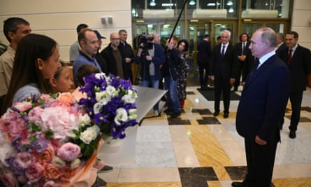A woman and child in the foreground hold bouquets as part of a group of people encircling Putin