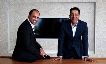 The Issa brothers pose for a publicity picture, with one leaning on a table and the other sitting on it