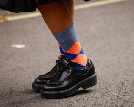 Closeup image of a woman wearing black shoes and checked socks walking along a street during the day.