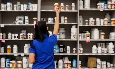 A pharmacist reaches for a drug bottle from the top shelf.