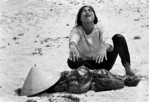 A Vietnamese woman cries over the body of her dead husband, whose body is wrapped in plastic. There is a hat covering the face.