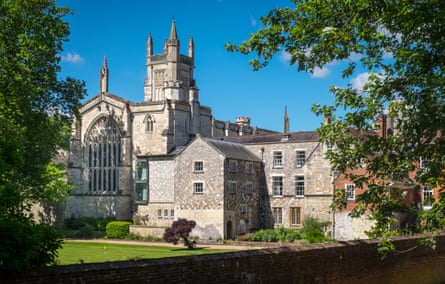 Tall mature trees surround a grassy area looking across to historic stone buildings including a chapel.