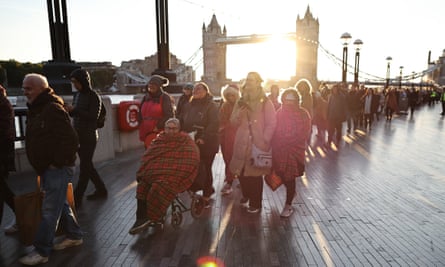 Sunrise behind Tower Bridge with a queue of people, one in a wheelchair with a blanket around their shoulders
