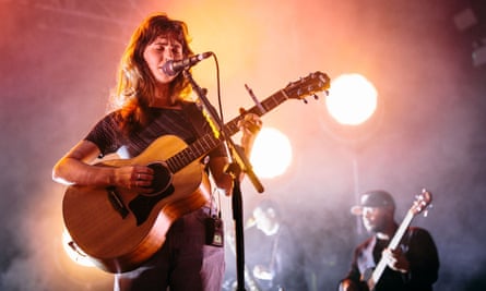A person plays an acoustic guitar and sings into a microphone onstage
