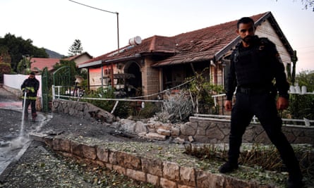 An Israeli police officer stands by as a firefighter putting out a fire after a rocket fired from Lebanon into Israel hit a residential house, in Rosh Pina.