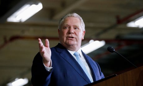 man wearing blue suit and light blue tie gestures while speaking behind microphone