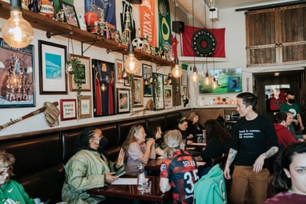 A bar, its walls filled with sports memorabilia, is full of customers.