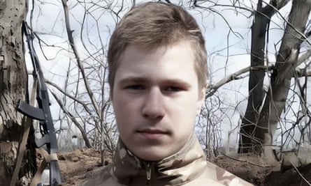 Daniil Yermolenko apparently in military uniform. A rifle is propped against a tree behind him