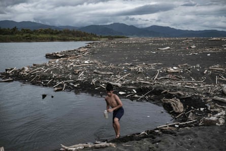 A young man collects water from a lagoon littered with plastic waste.