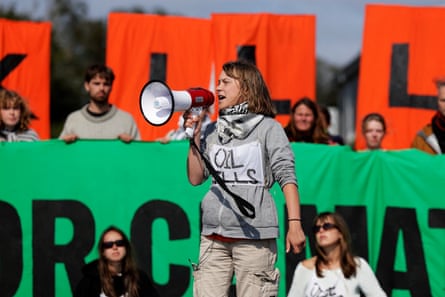 Greta Thunberg speaking through a megaphone wearing a sign that reads ‘Oil kills’