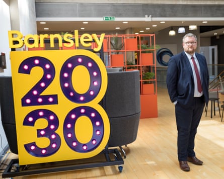 James Higginbottom in a suit stands next to a sign reading ‘Barnsley 2030’.