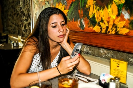 A teen rests her chin on her hand while she checks her flip phone