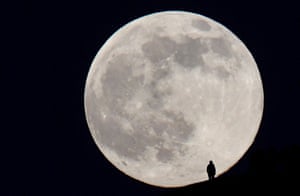 A person stands on the hillside of Glastonbury Tor as they watch the full moon