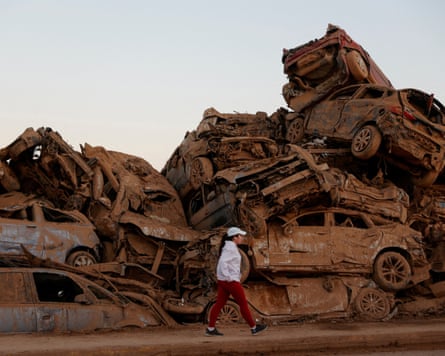 A person walks past a pile of crushed and muddy cars