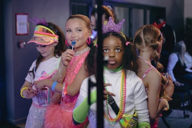 A group of young girls dressed up for a beauty contest, one of the licking a lollipop