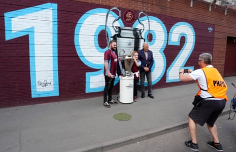 The former Aston Villa player Tony Morley poses with fans by a mural and the 1982 European Cup outside Villa Park before the Premier League match between Aston Villa and Spurs
