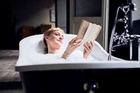 A relaxed woman taking a bubble bath and reading a book in a freestanding tub