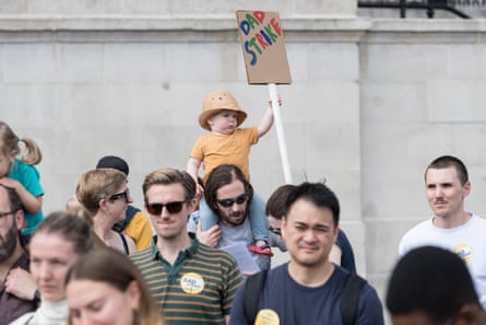 A young child holds up a placard from his father’s shoulders.